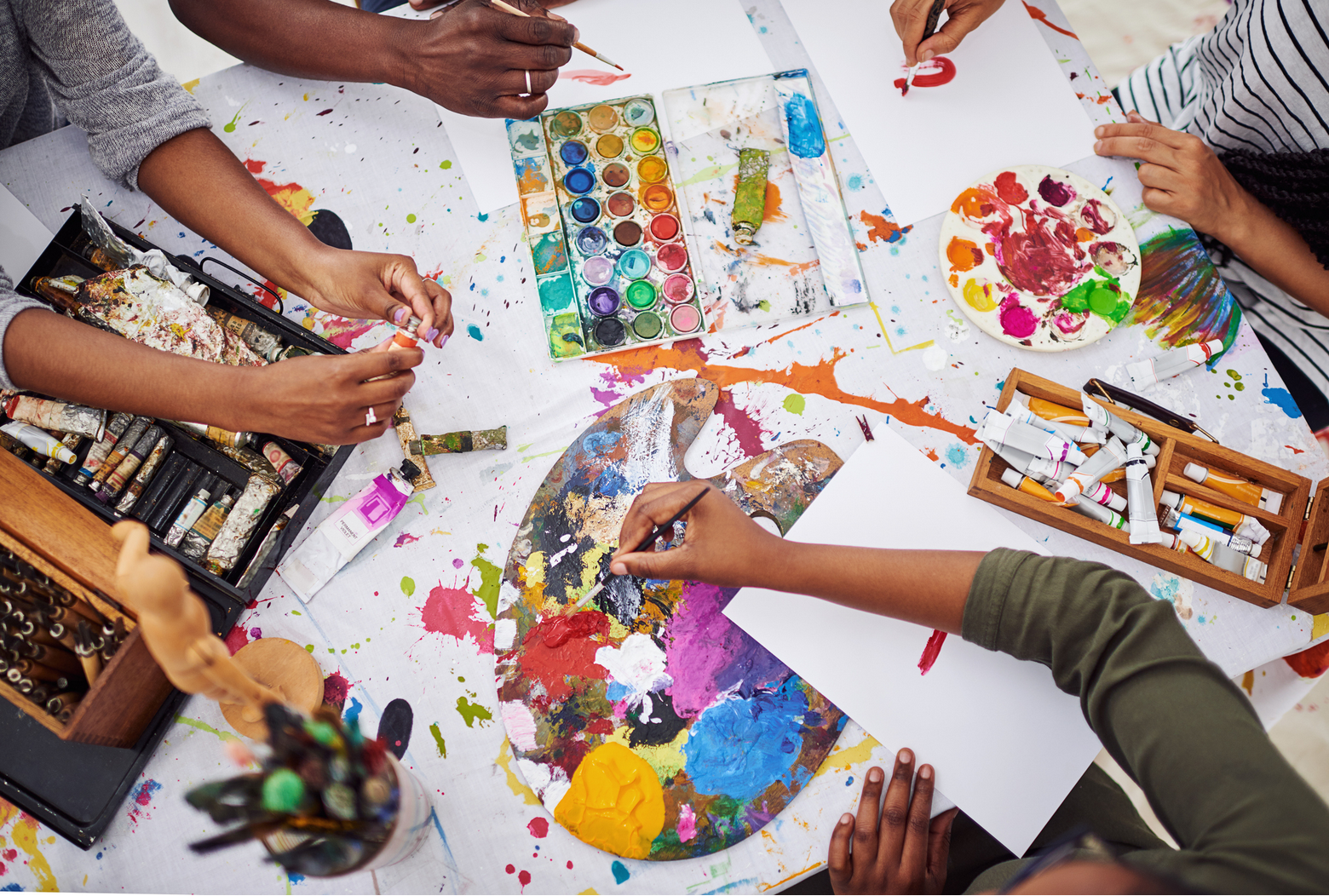 Ariel view of a table covered in art supplies and a few kids arms working on their paintings